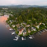 Scenic aerial view of waterfront homes, marina, lush greenery, and distant mountains during sunset.
